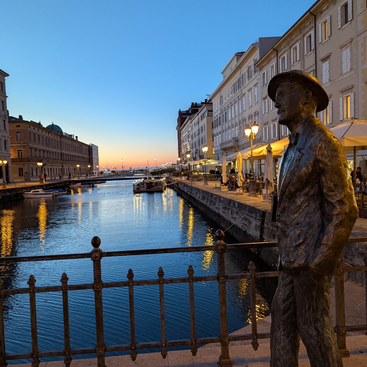 Une statue en bronze de James Joyce marche sur un pont, les quais sont occupés par des tonnelles et barnums. Les bâtiments sont nets, on sent que le quartier ou la ville est riche