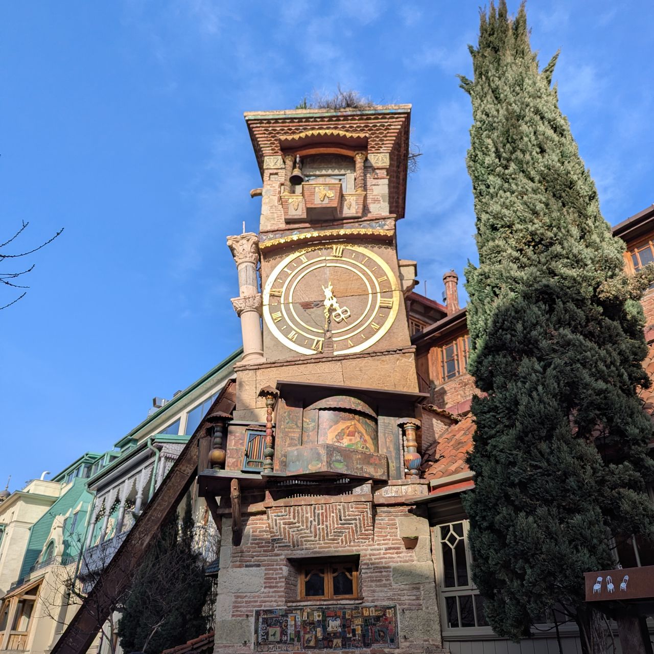 Photo d'une tour horloge marron toute biscornue, un des bâtiments emblématiques du Vieux Tbilissi.