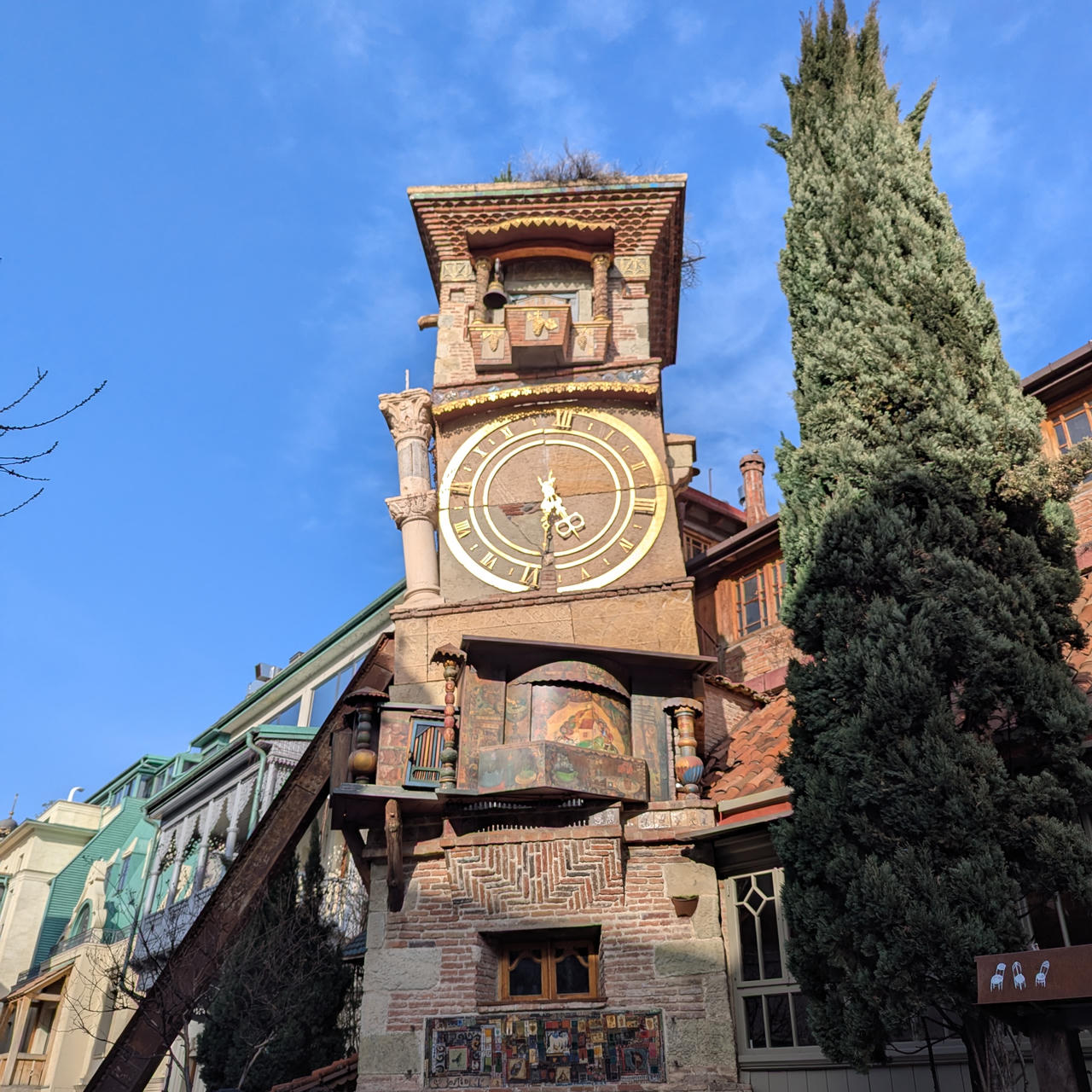 Photo d'une tour horloge marron toute biscornue, un des bâtiments emblématiques du Vieux Tbilissi.